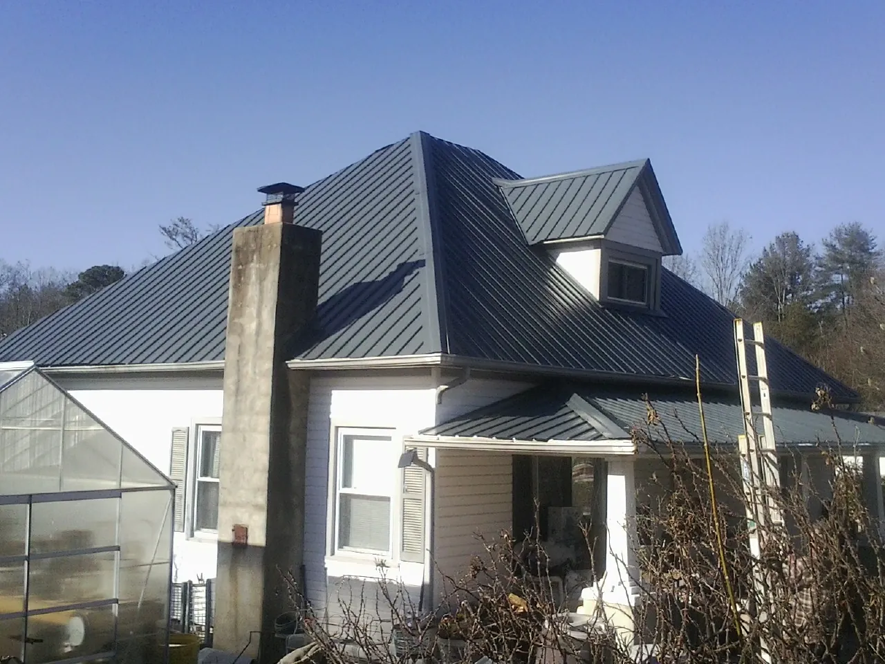 Dark blue standing seam metal roof on a white farmhouse with dormer — Slate & Tile Roof Repair by Roofing Brothers in Sun City