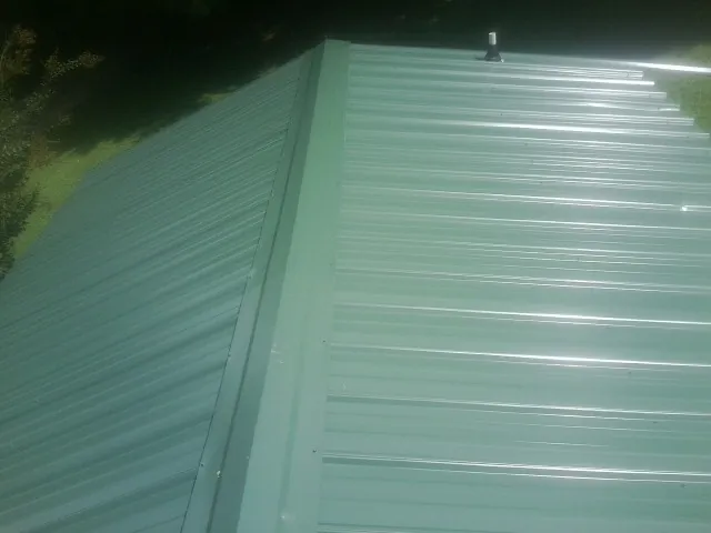 New green metal panels meeting at the ridge of a roof — Flat Roof Repair work by our crew in Sun City