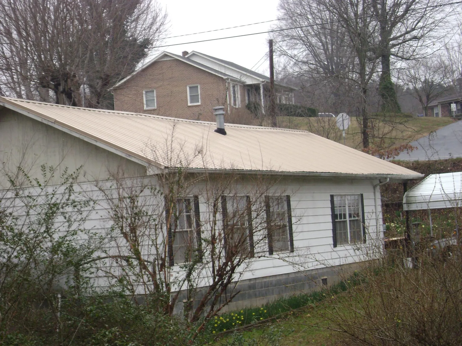 Tan metal roof on a white sided house set into a hillside — Commercial Roofing by Roofing Brothers in Sun City